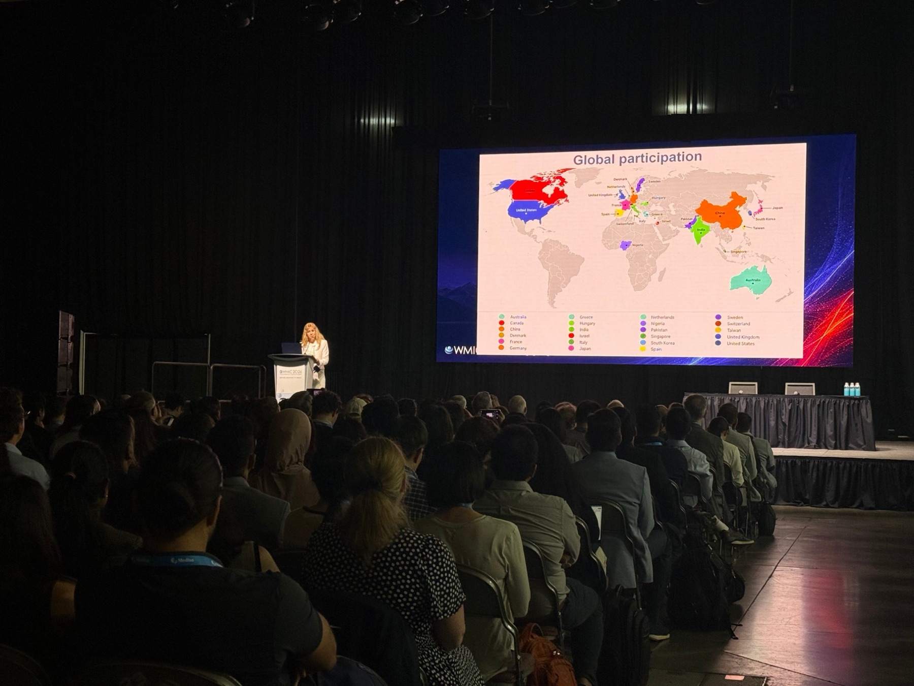 A speaker presenting a global participation map to a full room at WMIC